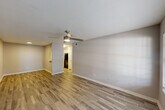 This single-story residence offers a functional and comfortable layout across two bedrooms, two bathrooms, a combined kitchen and living area, a closet, and a hallway. The living room features wood-look tile flooring, a ceiling fan with integrated lighting, and a window that allows natural light to fill the space. A pass-through window connects the living area to the kitchen, which is equipped with white cabinetry, light stone countertops, a stainless steel sink, and stainless steel appliances including a refrigerator and range. Adjacent to the kitchen is a dedicated dining area with matching flooring and a ceiling light fixture. Both bedrooms are carpeted and equipped with ceiling fans. The spacious primary bedroom includes a walk-in closet outfitted with built-in shelving, hanging rods, and a bench, providing generous storage. The bathrooms feature wood-look tile flooring, white vanity cabinetry, stone-topped counters, and well-lit mirrors. One bathroom includes a sliding closet door and a lighted vanity mirror. Throughout the residence, a neutral color palette of warm whites and soft grays creates a clean, cohesive aesthetic well-suited for a variety of interior styles.