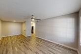 This single-story residence offers a functional and comfortable layout across two bedrooms, two bathrooms, a combined kitchen and living area, a closet, and a hallway. The living room features wood-look tile flooring, a ceiling fan with integrated lighting, and a window that allows natural light to fill the space. A pass-through window connects the living area to the kitchen, which is equipped with white cabinetry, light stone countertops, a stainless steel sink, and stainless steel appliances including a refrigerator and range. Adjacent to the kitchen is a dedicated dining area with matching flooring and a ceiling light fixture. Both bedrooms are carpeted and equipped with ceiling fans. The spacious primary bedroom includes a walk-in closet outfitted with built-in shelving, hanging rods, and a bench, providing generous storage. The bathrooms feature wood-look tile flooring, white vanity cabinetry, stone-topped counters, and well-lit mirrors. One bathroom includes a sliding closet door and a lighted vanity mirror. Throughout the residence, a neutral color palette of warm whites and soft grays creates a clean, cohesive aesthetic well-suited for a variety of interior styles.