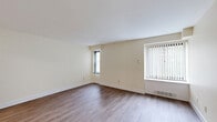 Located at 1199 Whitney Ave in Hamden, Connecticut, this one-bedroom, one-bathroom unit offers a well-organized layout across a single floor, comprising a living room, bedroom, kitchen, bathroom, and hallway. The living room is a bright, open space featuring warm hardwood-style flooring and two large windows dressed with vertical blinds, allowing generous natural light to fill the room. The kitchen is well-appointed with crisp white cabinetry, granite-style countertops, a stainless steel sink, and a white electric range with overhead ventilation — all set atop light wood-look flooring that adds warmth to the space. The bedroom is carpeted and comfortably sized, featuring a mirrored sliding closet door and a window with vertical blinds that brings in natural light while offering a sense of openness. The full bathroom is finished with floor-to-ceiling white tile, a toilet, a single vanity with a mirrored medicine cabinet, and a grab bar, providing a clean and functional design. A connecting hallway ties the rooms together efficiently. Throughout the unit, neutral wall tones and consistent finishes create a cohesive, move-in-ready atmosphere suited for comfortable everyday living.