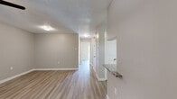 This single-floor residence offers a clean, contemporary design with a cohesive neutral color palette and light-toned luxury vinyl plank flooring that extends throughout the space. The open hallway connects the living areas seamlessly, with a granite countertop pass-through detail that adds a refined architectural touch between the kitchen and adjoining spaces.

The kitchen is a standout feature, showcasing white shaker-style cabinetry with brushed nickel hardware, granite countertops, a gray subway tile backsplash, and stainless steel appliances including an electric range. A window above the sink brings in natural light, enhancing the bright, functional layout.

The living area benefits from a sliding glass door that opens to an outdoor view of a lush green lawn, allowing abundant natural light to fill the room. A ceiling fan provides added comfort. The bedrooms are generously sized, each equipped with ceiling fans and windows fitted with blinds, contributing to a comfortable and airy atmosphere.

The bathroom is neatly finished with a granite-topped vanity, white cabinetry, and a full tub-shower combination with clean white tile surround. Textured ceilings are present throughout, and crisp white baseboards frame each room, completing the polished, move-in-ready feel of this thoughtfully updated space.