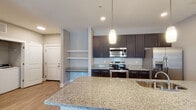 Located at 2545 Croquet Dr in Wilmington, NC, this single-floor residence offers a thoughtfully designed open-concept layout that seamlessly connects the kitchen, dining, and living areas. The kitchen is a standout feature, boasting dark espresso cabinetry, granite countertops, and a full suite of stainless steel appliances including a range, microwave, and refrigerator. A large central island with pendant lighting overhead provides additional prep space and casual seating, while built-in open shelving adds a functional and decorative touch. Wood-look flooring flows throughout the main living areas, enhancing the bright, airy atmosphere created by recessed lighting and natural light from well-placed windows. A dedicated laundry area is conveniently accessible from the main living space. The bathroom continues the home's modern aesthetic with a double-sink granite vanity, dark cabinetry with brushed nickel hardware, a walk-in glass shower, and wood-look flooring. The bedroom is carpeted for comfort and features a window that fills the room with natural light. The space as a whole presents a clean, contemporary design with a neutral color palette and quality finishes, making it an inviting and functional home in Wilmington.