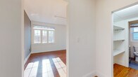 This 1-bedroom, 1-bathroom unit is thoughtfully designed to maximize functionality and comfort across a single floor. Rich hardwood flooring flows seamlessly throughout, lending warmth and continuity to every room. The open-concept kitchen and living area serves as the heart of the home, where a modern kitchen features two-tone cabinetry — white uppers paired with navy lowers — stainless steel appliances including a refrigerator, range, and microwave, and a clean white backsplash. Large windows bathe the combined space in generous natural light. The spacious primary bedroom offers ample room, a wall-mounted mini-split HVAC unit for climate control, and windows that invite in daylight and outdoor views. A dedicated closet with built-in white cabinetry provides practical storage. The bathroom is finished with crisp white subway tile and a glass-enclosed shower with brushed nickel hardware, creating a clean, contemporary feel. A connecting hallway ties the layout together efficiently. Throughout the unit, bright white walls, classic crown molding, and track lighting contribute to a light-filled, modern yet timeless aesthetic.