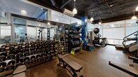 Located at 401 Thompson St in Ann Arbor, Michigan, this fitness facility offers a thoughtfully organized and fully outfitted workout environment on a single floor. The gym's industrial-inspired design is defined by an exposed dark ceiling with visible ductwork and structural elements, complemented by pendant lighting that casts a focused, energetic ambiance throughout the space.

Large windows along the perimeter walls allow natural light to fill the interior, creating an open and inviting atmosphere despite the compact footprint. The rubber flooring throughout provides both durability and comfort underfoot, making it well-suited for high-intensity training.

The strength training area is extensively equipped, featuring a full rack of dumbbells spanning a wide weight range, multiple kettlebells, medicine balls, and stability balls neatly organized on dedicated racks. Matrix-brand power racks and squat stations with Olympic barbells and weight plates anchor the free weights section. Adjustable benches are positioned throughout for versatile use.

On the cardio side, stair climbers and cable machines provide options for both cardiovascular conditioning and functional strength training. A glass partition wall with aluminum framing elegantly divides zones within the space, lending a modern, professional aesthetic. Wall mirrors enhance the sense of depth and allow users to monitor their form. The overall design is clean, purposeful, and optimized for a serious training experience.