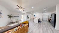 This single-story, one-bedroom, one-bathroom unit offers a thoughtfully designed open-concept layout with a clean, modern aesthetic. Light wood-style flooring runs throughout the entire space, complemented by crisp white walls and recessed lighting, creating a bright and cohesive atmosphere.

The combined living and kitchen area forms the heart of the unit. The living room is generously proportioned, featuring a ceiling fan with light fixture and direct access to an outdoor area through a front-facing door, allowing natural light to flow in. An arched architectural detail frames the transition between spaces, adding subtle character. The kitchen is equipped with gray cabinetry, black appliances including a refrigerator and range, and a white peninsula counter with bar seating for three, ideal for casual dining or entertaining.

Adjacent to the kitchen, a dedicated in-unit laundry area houses a full-size washer and dryer with overhead shelving. The spacious primary bedroom includes a ceiling fan, a window with natural light, and access to a closet. The bathroom features a combined tub and shower with tile surround, a vanity with dark cabinetry, and wood-style flooring that ties seamlessly to the rest of the unit.