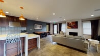 Located at 3508 NE 109th Ave in Vancouver, Washington, this contemporary single-floor space offers a thoughtfully designed open-concept layout that seamlessly connects its key functional areas. The interior is finished with large-format tile flooring throughout, complemented by recessed lighting and in-ceiling speakers that contribute to a polished, modern ambiance.

The kitchen is outfitted with rich dark wood cabinetry, stainless steel appliances including a gas range and French door refrigerator, a light-toned tile backsplash, and a white countertop island with bar seating. Striking copper pendant lights hang above the island, adding a warm, industrial accent to the space.

Adjacent to the kitchen, a dedicated dining area features a solid wood table with seating for several guests. The lounge area is generously proportioned, centered around a gray sofa and a sleek white coffee table, with a brick-surround fireplace serving as a focal point on one wall. Curated artwork and accent plants add character throughout.

A wall of windows dressed with dark curtains lines one side of the lounge, allowing ample natural light to filter in while maintaining a refined aesthetic. A glass-paneled entry door connects the interior to the exterior, enhancing the sense of openness.