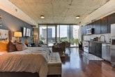 This single-floor studio unit at SkyHouse Buckhead in Atlanta, GA, offers a thoughtfully designed open-concept layout that seamlessly integrates the living, sleeping, and dining areas into one cohesive space. Rich hardwood flooring runs throughout, complemented by exposed concrete ceilings that lend an industrial-modern character to the interior.

The kitchen is well-appointed with dark espresso cabinetry extending to the ceiling, granite countertops, a white subway tile backsplash, and a full suite of stainless steel appliances, including a refrigerator with ice maker, electric range, built-in microwave, and dishwasher. A dedicated workspace area is conveniently positioned near a large window with city views.

Floor-to-ceiling windows and a private balcony flood the main living area with natural light and provide striking views of the Atlanta skyline. The sleeping area features a bold teal accent wall that anchors the space visually. The bathroom includes a soaking tub and shower combination with large-format marble-style tile surround and granite vanity. An in-unit washer and dryer and a walk-in closet with built-in shelving add practical convenience.