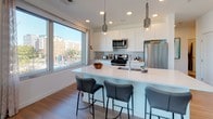 Located at 25 Lewis St in Boston's East Boston neighborhood, this single-floor residence showcases a contemporary design with an open, flowing layout and modern finishes throughout. Light wood flooring runs through the main living areas, complementing the clean, neutral palette and creating a cohesive aesthetic across the space.

The kitchen is a standout feature, outfitted with crisp white cabinetry, stainless steel appliances including a gas range, and a generous island with a white quartz countertop and seating for multiple guests. Pendant lighting and a large picture window offering neighborhood views complete the space. Adjacent to the kitchen, the dining area benefits from abundant natural light through oversized windows and is anchored by a striking sputnik chandelier.

The living room offers an inviting, open feel with windows framing city and waterfront views. Two well-appointed bedrooms provide comfortable retreats; one features a bold accent wall and bright window views, while the other showcases a tufted upholstered headboard and soft, neutral tones. The full bathroom includes a frameless glass shower, an extended double vanity, and tile flooring, while a separate half bath provides additional convenience.