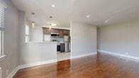 This single-floor unit offers a thoughtfully designed layout that balances modern updates with classic details. Rich, polished hardwood flooring flows throughout the main living areas and bedrooms, adding warmth and character to the space.

The open-concept kitchen and living area form the heart of the unit. The kitchen is equipped with stainless steel appliances, including a refrigerator, electric range, and over-the-range microwave. Dark, shaker-style cabinetry with brushed nickel hardware is paired with light countertops and a subtle subway tile backsplash, creating a sleek, contemporary aesthetic. A kitchen peninsula provides additional workspace and a natural boundary between the kitchen and the expansive living area.

The living room is generously proportioned, featuring recessed lighting and a large window that invites natural light and outdoor views into the space.

Two well-sized bedrooms each feature gleaming hardwood floors, ceiling fans, and multiple windows that fill the rooms with natural light. Radiator heating units are present in both bedrooms, reflecting the classic construction of the building.

The bathroom is finished with crisp white tile walls featuring a subtle textured pattern, gray slate-style floor tiles, a vanity, and a window that provides natural light and ventilation. The overall aesthetic throughout the unit is clean, neutral, and move-in ready.