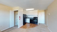 Located at 2805 N 47th Street in Philadelphia, PA, this single-floor unit offers a practical and well-organized layout designed for comfortable everyday living. The kitchen is a standout feature, outfitted with sleek black appliances including a refrigerator, electric range, and dishwasher, all complemented by crisp white cabinetry that provides ample storage space. A double-basin sink sits beneath overhead cabinets, making the kitchen both functional and efficient. The kitchen area transitions seamlessly from hardwood-style flooring into the adjacent carpeted living space, creating a clear and natural division between the cooking and relaxing zones. A walk-in closet offers generous storage, complete with built-in shelving and hanging rods, adding to the unit's practicality. The interior is finished in neutral tones throughout, with light-colored walls and ceilings that contribute to a bright and open atmosphere. Overhead fluorescent lighting in the kitchen ensures a well-lit workspace. The overall layout is compact yet thoughtfully designed, making efficient use of the available space while maintaining a clean, straightforward aesthetic suitable for a variety of lifestyles.