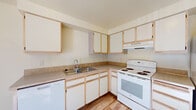 This single-floor, one-bedroom, one-bathroom residence offers a practical and well-organized layout. The kitchen is equipped with light wood-trimmed cabinetry providing ample upper and lower storage, laminate countertops, a stainless steel sink, a white electric range, dishwasher, and a full-size refrigerator. Warm wood-look vinyl flooring runs throughout the kitchen and dining area, which benefits from natural light and a ceiling fan overhead. The open living area features neutral carpet flooring, soft cream-toned walls, and a ceiling fan, creating a bright and airy atmosphere. Natural light filters in, adding warmth to the space. The bedroom is generously proportioned, featuring plush carpet, a window with blinds for natural light and privacy, and a sliding-door closet with a built-in hanging rod and shelf for organized storage. The bathroom includes a full tub and shower combo with a curved curtain rod, a toilet, a vanity with cabinet storage, and wood-look vinyl flooring that complements the rest of the home. The overall design is clean, neutral, and functional, making efficient use of every square foot.