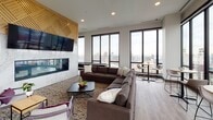 Located atop 240 Park Ave in Minneapolis, this sophisticated amenity lounge delivers a compelling blend of modern design and elevated urban living. The open-plan layout is anchored by floor-to-ceiling black-framed windows that frame sweeping panoramic views of the Minneapolis skyline, flooding the space with natural light throughout the day.

The lounge area features a striking marble fireplace wall with a mounted flat-screen TV, complemented by plush sectional sofas arranged for comfortable gathering. Adjacent to it, a dedicated games room hosts a billiards table alongside intimate café-style seating, all overlooking the city below.

At the heart of the space stands an expansive bar and kitchen island clad in dramatic veined marble countertops, surrounded by sleek bar stools — ideal for social entertaining. Overhead, an intricate geometric wood lattice ceiling structure adds warmth and an architectural focal point that distinguishes the bar area.

A formal dining area with a light wood table, modern pendant lighting, and direct access to an outdoor terrace provides a refined space for private gatherings. The terrace itself extends the living space outdoors with city views as a backdrop.

Throughout, wide-plank wood-tone flooring, curated artwork, and carefully selected furnishings tie together a cohesive, contemporary aesthetic that is both inviting and architecturally impressive.
