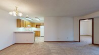 This single-floor residence offers a practical and well-organized layout designed for comfortable everyday living. The open-concept living and kitchen area forms the heart of the space, where a peninsula counter separates the two zones while maintaining a sense of openness. The kitchen is equipped with warm oak cabinetry extending to the upper and lower walls, white appliances including a coil-top electric range, double-basin sink, and refrigerator, all set against light countertops and tile flooring. A textured ceiling and flush fluorescent lighting illuminate the kitchen, while a chandelier adds a touch of warmth to the living area, which features neutral wall-to-wall carpeting throughout.

The bedrooms are generously sized, each carpeted and featuring windows with blinds that invite natural light. One bedroom includes a closet with sliding doors, providing practical storage. The two bathrooms are finished with light-toned cabinetry, wide vanity countertops, large mirrors with overhead lighting, and tile flooring. The overall aesthetic is clean and neutral, with consistent wood-toned trim accents, textured ceilings, and a straightforward design that offers a functional and move-in-ready living environment.