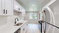 This single-floor, 3-bedroom, 2-bathroom home offers a thoughtfully designed layout that balances functionality and comfort. The renovated kitchen is a standout feature, showcasing crisp white shaker cabinetry with matte black hardware, quartz countertops, a subway tile backsplash, and a full suite of stainless steel appliances including a gas range, refrigerator, and dishwasher. Light hardwood-style flooring runs throughout the kitchen, which benefits from natural light through vertical-blind-fitted windows. The living areas are finished with warm neutral carpet, crown molding, and soft gray walls that create a calm, cohesive ambiance. Large sliding glass doors in the main living space flood the room with natural light and offer views of surrounding greenery. The bedrooms are carpeted and share the same neutral palette, with the generously sized primary bedroom providing ample space for furnishings. Three closets, including one with a built-in organization system featuring double hanging rods and shelving, provide excellent storage throughout. The bathrooms are clean and minimal in design. A dedicated entrance, central hallway, and efficient floor plan tie the entire home together into a cohesive and practical living space.