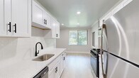 This single-floor, 3-bedroom, 2-bathroom home offers a thoughtfully designed layout that balances functionality and comfort. The renovated kitchen is a standout feature, showcasing crisp white shaker cabinetry with matte black hardware, quartz countertops, a subway tile backsplash, and a full suite of stainless steel appliances including a gas range, refrigerator, and dishwasher. Light hardwood-style flooring runs throughout the kitchen, which benefits from natural light through vertical-blind-fitted windows. The living areas are finished with warm neutral carpet, crown molding, and soft gray walls that create a calm, cohesive ambiance. Large sliding glass doors in the main living space flood the room with natural light and offer views of surrounding greenery. The bedrooms are carpeted and share the same neutral palette, with the generously sized primary bedroom providing ample space for furnishings. Three closets, including one with a built-in organization system featuring double hanging rods and shelving, provide excellent storage throughout. The bathrooms are clean and minimal in design. A dedicated entrance, central hallway, and efficient floor plan tie the entire home together into a cohesive and practical living space.