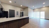 Located at 3080 East Cherry Street in Springfield, Missouri, this single-floor unit offers a clean, modern design with thoughtfully selected finishes throughout. The open-concept layout connects the kitchen and living area seamlessly, creating a bright and functional living space. Light wood-look flooring runs throughout the main areas, complementing the neutral gray walls and contemporary aesthetic.

The kitchen is equipped with dark espresso cabinetry, a granite-style countertop, and a large peninsula with an undermount sink — ideal for both meal prep and casual dining. Black appliances, including a refrigerator, range, and over-the-range microwave, provide a cohesive, modern look. A built-in electrical panel is conveniently recessed along the kitchen wall.

The living area is generously sized with tall ceilings that amplify the sense of openness. A sliding glass door fitted with vertical blinds allows natural light to fill the space and provides access to the outdoors.

The bedroom features plush carpet flooring, a bright window with blinds, and a dedicated closet with built-in shelving and hanging rods. The bathroom is finished with elegant marble-patterned tile flooring in a chevron layout, a dark vanity with a stone-top, and a full tub-shower combination — delivering a polished, move-in-ready feel.