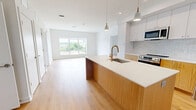 Located at 6320 Shakespeare Street in Pittsburgh's vibrant East Liberty neighborhood, this two-bedroom, two-bathroom residence offers a thoughtfully designed, modern interior. Light-toned hardwood flooring flows consistently throughout the unit, creating a warm and cohesive aesthetic against the crisp white walls.

The open-concept kitchen and living area serves as the heart of the home, anchored by a large center island with a natural wood base, white quartz countertop, and a sleek gold-finished faucet. Upper white cabinetry pairs with warm wood lower cabinets, complemented by classic white subway tile backsplash and stainless steel appliances. Pendant lighting adds a contemporary finish to the space.

Both bedrooms are generously proportioned, bathed in natural light through large sliding windows that frame elevated views of the Pittsburgh skyline and surrounding neighborhood, including a notable historic church steeple. Each bedroom includes dedicated closet space.

The two bathrooms are well-appointed with consistent finishes: one features a tiled tub-shower combination with a warm wood vanity and gray tile flooring, while the other offers a spacious glass-enclosed walk-in shower with white subway tile walls. Both bathrooms maintain a clean, modern aesthetic that aligns with the overall design of the unit.