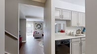 This two-story, 2-bedroom, 2-bathroom home is thoughtfully laid out across two well-proportioned floors. The main level hosts the primary living spaces, including a bright living room filled with natural light from large sliding glass doors that open to an outdoor patio. The kitchen is outfitted with gray cabinetry, white countertops, black appliances including a range, refrigerator, dishwasher, and over-the-range microwave, and features wood-look flooring. Adjacent to the kitchen, the dining area accommodates a dining table beneath a pendant light, with a large window allowing ample natural light. A hallway on the main level connects the living spaces to the staircase and a full bathroom, which includes a single vanity, toilet, and mirror. Upstairs, the two bedrooms are carpeted and offer a comfortable retreat. The spacious primary bedroom features a window with outdoor views and dedicated closet space with built-in shelving and hanging rods. The second bedroom is similarly well-sized. A second full bathroom serves the upper level. Neutral gray walls, wood-look flooring on the main level, and carpet upstairs create a cohesive and inviting atmosphere throughout.