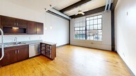 This contemporary apartment showcases a blend of industrial and modern aesthetics. The open-concept living area boasts high ceilings with exposed beams and ductwork, complemented by large windows that flood the space with natural light. The kitchen features sleek stainless steel appliances and dark wood cabinetry. Both bedrooms offer ample space, with the primary bedroom measuring 170 sq ft. The bathrooms are outfitted with modern fixtures, including granite countertops and spacious showers. Hardwood floors run throughout the unit, adding warmth to the industrial design. The apartment's 860 sq ft layout efficiently utilizes space, creating a comfortable and stylish urban living environment.