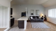 Located at 2486 N Harbor Dr in Bay City, Michigan, this single-floor home offers a well-organized layout with notable architectural character throughout. The open-concept living and kitchen area serves as the heart of the home, anchored by soaring vaulted ceilings that lend a sense of spaciousness and airiness. Large windows fitted with vertical blinds allow ample natural light to fill the living room, which features plush carpeting and a welcoming atmosphere. The kitchen is appointed with striking dark cabinetry, light granite countertops, a kitchen island with bar-height seating, and black appliances, including a range and refrigerator — creating a bold, modern contrast. The two bedrooms are carpeted and generously proportioned, each featuring large windows that provide outdoor views and abundant natural light. Both bedrooms include walk-in closets with built-in shelving for practical storage. The vaulted ceiling detail carries into at least one of the bedrooms, further enhancing its sense of volume. The full bathroom features a wide vanity with a large mirror, ample counter space, and a shower-tub combination. Durable hardwood-style flooring in the kitchen and entryway transitions seamlessly to soft carpet in the living and sleeping areas, rounding out this comfortable and functional home.