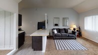 Located at 2486 N Harbor Dr in Bay City, Michigan, this single-floor home offers a well-organized layout with notable architectural character throughout. The open-concept living and kitchen area serves as the heart of the home, anchored by soaring vaulted ceilings that lend a sense of spaciousness and airiness. Large windows fitted with vertical blinds allow ample natural light to fill the living room, which features plush carpeting and a welcoming atmosphere. The kitchen is appointed with striking dark cabinetry, light granite countertops, a kitchen island with bar-height seating, and black appliances, including a range and refrigerator — creating a bold, modern contrast. The two bedrooms are carpeted and generously proportioned, each featuring large windows that provide outdoor views and abundant natural light. Both bedrooms include walk-in closets with built-in shelving for practical storage. The vaulted ceiling detail carries into at least one of the bedrooms, further enhancing its sense of volume. The full bathroom features a wide vanity with a large mirror, ample counter space, and a shower-tub combination. Durable hardwood-style flooring in the kitchen and entryway transitions seamlessly to soft carpet in the living and sleeping areas, rounding out this comfortable and functional home.