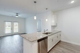 This single-story unit offers a thoughtfully designed layout across three bedrooms and two bathrooms. The open-concept kitchen and living area forms the heart of the home, where a granite-topped island with pendant lighting serves as a natural focal point. The kitchen is well-equipped with white shaker cabinetry, a subway tile backsplash, and a full suite of stainless steel appliances, including a refrigerator, range, microwave, and dishwasher. The adjoining living area features wood-look plank flooring and a ceiling fan, with natural light entering through a set of glass panel doors that overlook a grassy outdoor area.

The bedrooms continue the clean aesthetic with the same wood-look flooring, ceiling fans, and neutral white walls. The primary bedroom includes a window with outdoor views. Both bathrooms are finished with white cabinetry, granite-topped vanities, and full tub-shower combinations with brushed nickel fixtures. A connecting hallway links the bedrooms and bathrooms efficiently. Throughout the unit, the consistent use of neutral tones, granite surfaces, and modern fixtures creates a cohesive and contemporary ambiance.
