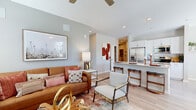 This single-story unit offers a thoughtfully designed open-concept floor plan that efficiently connects the living, dining, and kitchen areas into one cohesive space. Light-toned luxury vinyl plank flooring runs throughout the main areas, complemented by neutral walls and recessed lighting that create a bright, contemporary atmosphere. A ceiling fan anchors the living room, which receives natural light through multiple windows fitted with blinds and sheer curtains offering views of the surrounding neighborhood.

The kitchen is a functional centerpiece, equipped with stainless steel appliances including a French door refrigerator, gas range, and microwave. White shaker-style cabinetry pairs with a granite-topped island that provides bar seating for two, seamlessly connecting to the dining area.

The bedroom features plush carpet, a walk-in closet with built-in shelving and hanging rods, and direct access to one of three bathrooms. The primary bathroom includes a granite vanity with white cabinetry and a tub-shower combination with tile surround. A dedicated laundry room accommodates a full-size washer and dryer with additional open shelving for storage.
