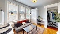 Located at 487 Prentis St in Detroit's vibrant Midtown neighborhood, this thoughtfully laid-out single-floor unit offers a functional and comfortable living experience across its compact footprint. The living area greets you with warm hardwood floors, soft gray walls, and a bank of double-hung windows fitted with wooden blinds that fill the space with abundant natural light and views of the surrounding neighborhood. A built-in desk nook seamlessly integrated into the living room provides a dedicated workspace, making efficient use of every square foot. The layout flows from the living area into a modest but well-appointed kitchen, visible through a boldly framed doorway that adds a modern design contrast. The bedroom is an intimate retreat, featuring a window with neighborhood views, rich hardwood flooring, and clean, light gray walls that create a calm and restful atmosphere. The bathroom is finished with classic white subway-style wall tiles and includes a bathtub with a frosted glass window that allows natural light while maintaining privacy. Throughout the unit, consistent hardwood flooring, neutral tones, and thoughtful design details create a cohesive and inviting ambiance well-suited to urban living in one of Detroit's most walkable and culturally rich districts.