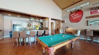 Located at 5353 Wilcox Rd in Dublin, Ohio, this single-floor gathering space blends rustic charm with functional amenities, making it an inviting venue for events and recreation. The open main area commands attention with soaring vaulted ceilings and rich hardwood flooring, anchored by a full-size billiards table at its center. Pendant lighting with an industrial character illuminates the adjacent wet bar, which features a raised counter with seating, white cabinetry, and a decorative tile backsplash — ideal for entertaining.

The lounge area offers generous seating, including a tufted velvet sofa and classic wingback armchairs, with a cozy chess nook tucked nearby beneath a statement floor lamp. Large windows on one side of the lounge invite natural light and provide views of the surrounding outdoor landscape.

A defining feature of the space is its striking wall décor — an eclectic collection of vintage farmstand and orchard signs, including a large painted apple and antique advertising boards, that lend the interior a warm, nostalgic character rooted in local agricultural heritage.

The fully equipped kitchen includes white cabinetry, dark granite countertops, a diagonal tile backsplash, tile flooring, a full-size refrigerator, and built-in appliances. A transitional hallway connects the kitchen to the main gathering area, completing this well-appointed, character-rich space.