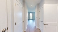 Located at 7 Crown Dr in Quincy, MA, this efficiently designed single-floor unit offers a thoughtfully laid-out living space. The open-concept kitchen and living room area is anchored by a modern kitchen outfitted with white flat-panel cabinetry, light-toned countertops, and a full suite of stainless steel appliances, including a refrigerator with ice maker, wall oven, built-in microwave, dishwasher, and a cooktop. Light hardwood-style flooring runs throughout, complementing the cool gray-blue walls and crisp white trim that define the unit's clean, contemporary aesthetic. The living area benefits from multiple windows that invite generous natural light and offer views of the surrounding neighborhood, with a glass-panel door providing additional brightness and outdoor access. The full bathroom features a warm wood-toned vanity with an integrated sink, light tile-style flooring, and a full bathtub with a curved shower curtain rod, along with accessibility grab bars. A dedicated closet provides practical storage. The unit's modern finishes, neutral palette, and well-appointed kitchen make it a functional and inviting space in the Quincy, MA area.