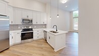 Located at 21501 Hickory St in Cornelius, NC, this one-bedroom, one-bathroom residence offers a thoughtfully designed layout with modern finishes throughout. The open-concept kitchen serves as a centerpiece of the living space, showcasing crisp white shaker cabinetry, a gray subway tile backsplash, quartz countertops, and a peninsula with an undermount sink and matte black faucet. Pendant lighting adds a contemporary touch, while stainless steel appliances — including a side-by-side refrigerator with ice maker, electric range, microwave, and dishwasher — provide full functionality. Light-toned hardwood-style flooring runs through the kitchen and main living area, complementing the bright, neutral palette.

The bedroom features soft carpeting, soaring ceilings, and a striking floor-to-ceiling multi-pane window that floods the room with natural light and offers views to the exterior. A dedicated closet provides ample storage. The bathroom is finished with light hardwood-style flooring, a full soaking tub and shower combination with white subway tile surround, and matte black fixtures that echo the design language found throughout the unit. The overall ambiance is clean, modern, and move-in ready.