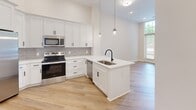 Located at 21501 Hickory St in Cornelius, NC, this one-bedroom, one-bathroom residence offers a thoughtfully designed layout with modern finishes throughout. The open-concept kitchen serves as a centerpiece of the living space, showcasing crisp white shaker cabinetry, a gray subway tile backsplash, quartz countertops, and a peninsula with an undermount sink and matte black faucet. Pendant lighting adds a contemporary touch, while stainless steel appliances — including a side-by-side refrigerator with ice maker, electric range, microwave, and dishwasher — provide full functionality. Light-toned hardwood-style flooring runs through the kitchen and main living area, complementing the bright, neutral palette.

The bedroom features soft carpeting, soaring ceilings, and a striking floor-to-ceiling multi-pane window that floods the room with natural light and offers views to the exterior. A dedicated closet provides ample storage. The bathroom is finished with light hardwood-style flooring, a full soaking tub and shower combination with white subway tile surround, and matte black fixtures that echo the design language found throughout the unit. The overall ambiance is clean, modern, and move-in ready.