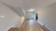 Located at 14040 Dana Ave in Philadelphia, PA, this 2-bedroom, 1-bathroom home offers a clean, functional layout with consistent neutral gray walls and white trim throughout. The open living area is highlighted by durable hardwood-style flooring, a large window that fills the space with natural light, and an arched entryway that adds a subtle architectural detail connecting to the kitchen. The kitchen features white cabinetry, granite-look countertops, a stainless steel refrigerator, dishwasher, and stove, all arranged along a galley-style corridor with light wood flooring. Both bedrooms are carpeted in soft neutral tones and offer ample space, with the generously sized primary bedroom featuring a window with outdoor views. The second bedroom includes a built-in closet with paneled double doors, providing practical storage. The bathroom is equipped with a full tub and shower combination with clean white tile surround and chrome fixtures. A dedicated utility room and additional closet round out the home's storage options. A staircase with a white metal railing is visible, indicating access to the entry level. The overall ambiance is clean, bright, and move-in ready.