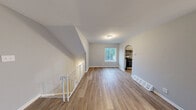 Located at 14040 Dana Ave in Philadelphia, PA, this 2-bedroom, 1-bathroom home offers a clean, functional layout with consistent neutral gray walls and white trim throughout. The open living area is highlighted by durable hardwood-style flooring, a large window that fills the space with natural light, and an arched entryway that adds a subtle architectural detail connecting to the kitchen. The kitchen features white cabinetry, granite-look countertops, a stainless steel refrigerator, dishwasher, and stove, all arranged along a galley-style corridor with light wood flooring. Both bedrooms are carpeted in soft neutral tones and offer ample space, with the generously sized primary bedroom featuring a window with outdoor views. The second bedroom includes a built-in closet with paneled double doors, providing practical storage. The bathroom is equipped with a full tub and shower combination with clean white tile surround and chrome fixtures. A dedicated utility room and additional closet round out the home's storage options. A staircase with a white metal railing is visible, indicating access to the entry level. The overall ambiance is clean, bright, and move-in ready.