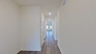 This single-story home presents a clean, modern design highlighted by consistent wood-look flooring throughout the main living areas and neutral white walls that create a bright, cohesive aesthetic. A long hallway connects the various rooms, lined with recessed lighting and smooth white walls that contribute to an open, airy feel.

The living area is generously sized, featuring multiple windows that allow abundant natural light to fill the space, complemented by wood-look flooring and a door providing exterior access. The kitchen is well-appointed with white shaker-style cabinetry extending to the ceiling, granite countertops across both the perimeter surfaces and a central island with an integrated sink, and stainless steel appliances including a range and over-the-range microwave.

The bedrooms feature plush carpeting and windows offering natural light, with closets equipped with wire shelving systems for organized storage. The primary bathroom includes a glass-enclosed shower, white vanity cabinetry with a clean countertop, and direct access to a spacious walk-in closet. A secondary bathroom offers a full tub-shower combo, toilet, and matching white vanity. The attached two-car garage provides ample space with an automatic opener.