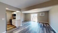 This single-floor unit offers a clean, modern design defined by consistent luxury vinyl plank flooring in a cool grey-blue tone that flows seamlessly throughout the entire space. The open-concept living and kitchen area is bright and spacious, with neutral taupe walls and white trim creating a contemporary, cohesive aesthetic. A sliding glass door in the living area fills the space with natural light while providing direct access to a private balcony with outdoor views.

The kitchen is efficiently designed with crisp white cabinetry, granite-look countertops, and a full suite of stainless steel appliances including a range, microwave, and dishwasher. The kitchen opens visually to the main living area through a generous archway, supporting an easy flow between spaces.

The entryway is practical and welcoming, featuring multiple doors — including a closet — and recessed lighting overhead. The bedroom is well-proportioned, equipped with a ceiling fan and light fixture, a window with blinds for natural light, and a baseboard heating unit. The bathroom is neatly finished with a full tub and shower surround, a white vanity with a single sink, brushed nickel fixtures, and a framed mirror. A wall-mounted HVAC unit in the living room provides additional climate control. Overall, the unit presents a fresh, move-in-ready condition with thoughtful, functional finishes throughout.