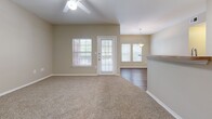 Located in Kyle, TX, this well-appointed 3-bedroom, 2-bathroom unit offers a practical and comfortable single-floor layout. The living area features plush carpeting, a ceiling fan, and large windows and a glass door that invite abundant natural light, with direct access to a covered balcony framed by mature trees. The kitchen is equipped with warm wood-toned cabinetry, laminate countertops, white appliances including a range and refrigerator, and durable hardwood-style flooring. A pendant light over the adjacent dining area adds a welcoming touch.

Each of the three bedrooms is finished with soft carpeting, neutral beige walls, ceiling fans, and windows offering outdoor views. The primary bedroom provides a generous footprint with a closet. The two bathrooms are consistently appointed with wood-style flooring, oak vanities with laminate countertops, and full tub-shower combinations with white tile surrounds. Two hallways connect the spaces efficiently throughout the unit.

The covered balcony, accessible through a distinctive red front door, features a decorative iron railing and overlooks a tree-lined setting, providing a pleasant outdoor retreat. The overall design is clean, neutral, and move-in ready.