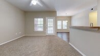 Located in Kyle, TX, this well-appointed 3-bedroom, 2-bathroom unit offers a practical and comfortable single-floor layout. The living area features plush carpeting, a ceiling fan, and large windows and a glass door that invite abundant natural light, with direct access to a covered balcony framed by mature trees. The kitchen is equipped with warm wood-toned cabinetry, laminate countertops, white appliances including a range and refrigerator, and durable hardwood-style flooring. A pendant light over the adjacent dining area adds a welcoming touch.

Each of the three bedrooms is finished with soft carpeting, neutral beige walls, ceiling fans, and windows offering outdoor views. The primary bedroom provides a generous footprint with a closet. The two bathrooms are consistently appointed with wood-style flooring, oak vanities with laminate countertops, and full tub-shower combinations with white tile surrounds. Two hallways connect the spaces efficiently throughout the unit.

The covered balcony, accessible through a distinctive red front door, features a decorative iron railing and overlooks a tree-lined setting, providing a pleasant outdoor retreat. The overall design is clean, neutral, and move-in ready.