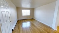 This single-floor space presents a clean, straightforward layout designed for comfort and functionality. The interior is characterized by beautifully polished hardwood floors that run throughout, reflecting natural light and adding warmth to the overall atmosphere. The walls are finished in a soft, neutral beige tone, creating a calm and versatile backdrop suitable for a variety of uses and décor styles. A prominent window allows ample natural light to fill the room, enhancing the open and airy feel of the space. The ceiling features a subtle textured finish, adding a modest architectural detail overhead. A baseboard heating unit runs along the exterior wall beneath the window, providing an efficient and unobtrusive climate control solution. Crisp white baseboards frame the perimeter of the room, offering a clean contrast against the warm hardwood floors. Electrical outlets are conveniently positioned along the walls, contributing to the room's practical design. The overall ambiance is bright, tidy, and move-in ready, making it a versatile space well-suited for residential living. The single-floor layout ensures easy accessibility and a cohesive flow throughout the entire unit.