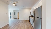This single-floor apartment offers a well-designed, open-concept layout that seamlessly connects the kitchen, living, and dining areas. The unit is finished with durable wood-look flooring that flows consistently throughout every room, contributing to a cohesive and contemporary aesthetic.

The kitchen is equipped with a full suite of stainless steel appliances, including a refrigerator, electric range, and over-the-range microwave. Two-tone cabinetry — white upper cabinets paired with light gray lower cabinets — frames granite-style countertops with an undermount sink, providing ample storage and prep space.

The open living area benefits from natural light through a window fitted with horizontal blinds, and is climate-controlled via a wall-mounted HVAC unit. A ceiling fan with integrated lighting is installed overhead, serving both the kitchen and living zones.

The bedroom is a spacious, light-filled room with its own ceiling fan, a window with blinds, and a wall-mounted HVAC unit for individual climate control. The bathroom features wood-look flooring, a granite-topped vanity with under-sink storage, a toilet, and a full-size tub/shower combination with a white surround. A stackable washer and dryer unit is conveniently located within the unit. The front entry door includes a sidelight window, allowing natural light into the entryway.