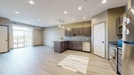 This well-appointed single-floor residence offers a thoughtfully designed open-concept layout that seamlessly connects the kitchen and living area. The kitchen is a standout feature, showcasing rich dark-stained cabinetry, granite countertops, and a full suite of stainless steel appliances, including a refrigerator, electric range, over-the-range microwave, and dishwasher. Pendant lighting above the peninsula adds a refined touch, while recessed ceiling lights illuminate the space throughout. Light-toned luxury vinyl plank flooring extends across the main living areas, providing a clean and contemporary aesthetic. The living area benefits from natural light streaming in through a sliding glass door that opens to a private balcony, offering outdoor views. The bedroom features plush wall-to-wall carpeting and a window with natural light and outdoor views, creating a comfortable and restful retreat. The bathroom is finished with wood-look tile flooring, neutral wall tones, and chrome hardware accoutrements. A dedicated in-unit laundry room houses a full-size top-loading washer and dryer with wire shelving above for additional storage. The overall design palette of warm neutrals, modern finishes, and practical amenities makes this a functional and stylish living space.