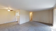 This single-floor unit offers a practical and comfortable layout designed for everyday living. The spacious living area is finished with wall-to-wall carpet in a neutral tone, warm beige walls, and a ceiling fan overhead. A baseboard heating system runs along the perimeter, ensuring year-round comfort. Large sliding glass doors open to an outdoor balcony, flooding the room with natural light and offering pleasant views of surrounding greenery. The semi-open kitchen is positioned just off the living area, featuring white cabinetry and a clean, functional design. A partial dividing wall separates the kitchen from the living space, maintaining a sense of openness while defining each zone. A hallway connects the main living area to the private quarters, leading to a well-sized bedroom with a window that brings in abundant natural light and frames views of the outdoors. Baseboard heating is also present in the bedroom for added comfort. The bathroom features a wide vanity with a light stone-patterned countertop, an undermount sink, large mirror, bright overhead lighting, and tile flooring, providing a clean and functional space. Overall, the unit presents a straightforward, move-in-ready layout with consistent finishes throughout.