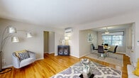 This single-floor residence offers a thoughtfully arranged layout that seamlessly connects its main living areas. Warm hardwood flooring flows throughout the living room, dining area, and bedroom, creating a cohesive and inviting atmosphere. The living room is generously proportioned, featuring large windows that draw in abundant natural light and a wall-mounted mini-split system for efficient climate control. The space opens directly into the dining area, which is highlighted by a glass-top table, upholstered seating, and a wide window overlooking lush greenery outside.

The kitchen is equipped with rich, dark-stained raised-panel cabinetry extending to the upper walls, light stone-patterned countertops, a double sink, and black appliances including an electric range and refrigerator. Tile flooring and a window provide practicality and brightness to the workspace.

The bedroom continues the hardwood flooring and includes a second mini-split unit, a window with exterior views, and a closet. The bathroom features white tile wainscoting, a vanity with wood cabinetry, tile flooring, and a shower-tub combination, maintaining a clean and functional aesthetic throughout.