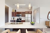 This thoughtfully designed 2-bedroom, 2-bathroom residence in Council Bluffs, Iowa offers a contemporary open-concept layout that seamlessly connects the kitchen, dining area, and living room. The kitchen is equipped with rich dark-wood cabinetry, stainless steel appliances, and a generous island with a white quartz countertop and bar seating, illuminated by modern pendant lighting. The adjoining dining and living areas are bathed in natural light from expansive floor-to-ceiling windows and a sliding glass door that opens to a private balcony, offering open outdoor views. The living room features light hardwood-style flooring and a ceiling fan. The spacious primary bedroom includes plush carpeting, a large window with exterior views, and access to a well-proportioned walk-in closet with built-in shelving. The second bedroom is equally comfortable with similar finishes and natural light. Two clean, modern bathrooms feature light wood-tone flooring and walk-in showers. Additional highlights include an in-unit laundry area, a hallway connecting the private spaces, and ample closet storage throughout. The overall ambiance is bright, clean, and contemporary.