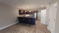 Kennedy Place is a well-designed two-story residence that combines modern finishes with functional living spaces across both floors. The main level features an open-concept layout anchored by a standout kitchen, complete with rich dark cabinetry, granite countertops, a full suite of stainless steel appliances including a range, microwave, refrigerator, and dishwasher. A large center island with seating for multiple bar stools serves as a natural gathering point, illuminated by elegant pendant lighting and complemented by recessed ceiling lights throughout. Durable wood-look flooring flows seamlessly across the main level, adding warmth and continuity to the space. The entry area opens into a spacious living room fitted with a ceiling fan and a large window that brings in natural light and neighborhood views. A conveniently located bathroom on the main level features matching dark cabinetry and wood-look flooring. Upstairs, the bedrooms are carpeted for comfort and include ceiling fans and multiple windows that frame exterior views. The upper-level bathrooms are clean and functional, with one featuring a full tub-shower combination. Neutral tones and consistent finishes throughout create a cohesive, move-in ready aesthetic.