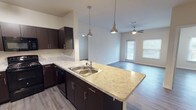 This single-floor, two-bedroom, two-bathroom unit features a thoughtfully designed open-concept layout that seamlessly connects the kitchen and living area. The kitchen is equipped with rich dark cabinetry, light granite-style countertops, black appliances including a refrigerator, electric range, and microwave, and a peninsula with a double stainless steel sink illuminated by stylish pendant lighting. Track lighting overhead adds a modern touch. The living area is bright and welcoming, featuring wood-style flooring, neutral-toned walls, a ceiling fan, and a windowed door that allows natural light to fill the space. Both bedrooms are comfortably sized with wood-style flooring, ceiling fans, and easy access to closet space. Each bedroom offers a calm, neutral palette and connects conveniently to the rest of the unit. The two bathrooms each include a soaking tub and shower combination with white tile surrounds, curved chrome curtain rods, and clean, simple finishes. Throughout the unit, consistent wood-style flooring, neutral walls, and practical fixtures create a cohesive and functional living environment suited for everyday comfort.