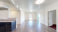 Located on Alexander Street in Gilroy, California, this single-floor unit offers a thoughtfully designed layout with a clean, contemporary aesthetic throughout. The open-concept living and dining area is a standout feature, finished with smooth hardwood-style flooring that reflects natural light streaming in through multiple windows and a sliding glass door. The bright, white walls and flush-mount lighting contribute to an airy, welcoming atmosphere.

The kitchen is positioned adjacent to the living area and features dark navy cabinetry with granite-style countertops, a black electric range, a built-in dishwasher, an under-cabinet range hood, and a stainless steel sink. A peninsula counter provides a natural transition between the kitchen and the main living space.

Bedrooms are carpeted in a deep burgundy tone, each offering generous built-in closets with wire shelving for organized storage. Natural light reaches the bedrooms through slatted-blind windows. The bathroom is cleanly finished with wood-style tile flooring, a full soaking tub with a tiled surround, a shower rod, and a wall-mounted grab bar.

A private balcony, accessible via sliding glass doors from the living area, delivers expansive views of the surrounding Gilroy landscape and the scenic hills beyond — a notable outdoor feature of this unit.