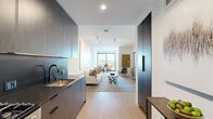 This thoughtfully designed single-floor residence offers a cohesive modern aesthetic across its efficiently arranged layout. Light oak hardwood flooring flows throughout, connecting each area seamlessly and contributing to a warm, contemporary feel.

The kitchen is outfitted with floor-to-ceiling dark wood cabinetry, dark stone countertops, a matte black faucet, a stainless steel undermount sink, and a matching dark tile backsplash. Integrated appliances, including a gas range and refrigerator, maintain the kitchen's streamlined, handleless design.

The open living and dining area extends toward a large floor-to-ceiling window and glass door, inviting natural light deep into the space while framing expansive city views. This area provides comfortable room for both a seating arrangement and a dining table.

The bedroom features soft, neutral tones and a dedicated window with broad city views. A cozy seating nook beside the window maximizes the panoramic outlook. A ceiling fan adds practical comfort to the serene, light-filled space.

The bathroom showcases full marble-style stone tile walls and flooring within a glass-enclosed walk-in shower, complemented by a matte black overhead rain showerhead and matching black hardware, delivering a refined, spa-like finish throughout.
