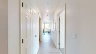 Located at 414 22nd St in Richmond, CA, this single-floor unit presents a well-organized layout connecting key living spaces through a bright, white-walled hallway finished with light wood-style flooring. The corridor leads directly into an open living and dining area, where large windows allow natural light to fill the room and provide views of the surrounding neighborhood. Flush-mount ceiling fixtures supplement the natural light, creating a consistently well-lit environment. The living area comfortably accommodates both a seating arrangement and a dining set, making efficient use of the available space.

The kitchen features rich dark walnut-toned cabinetry on both upper and lower levels, paired with light-colored countertops. It is equipped with a black range and oven, an overhead exhaust hood, and a single-basin sink, offering a functional cooking space with ample storage.

The bathroom is finished with matching dark wood cabinetry beneath a single vanity with a wide mirror and overhead lighting. A full soaking tub with a shower curtain enclosure completes the space, all set on light wood-style flooring.

The bedroom is a calm, simply appointed room with neutral walls, carpeted flooring, and a wall-mounted split AC unit, ensuring year-round comfort. The cohesive design and light palette give the entire unit a clean, modern ambiance.