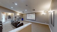 Located in El Cajon, CA, this purpose-built home theater delivers a true cinema experience within a thoughtfully designed single-floor layout. The main screening room is the heart of the space, finished with warm neutral-toned walls, recessed ceiling lighting, and wall-mounted sconce lighting that creates an atmospheric, theater-like ambiance. Plush, wall-to-wall carpet in a neutral tone runs throughout, adding comfort underfoot and contributing to the room's acoustic quality.

The seating arrangement consists of multiple rows of dark leather recliner chairs with built-in cup holders, configured in a tiered, stadium-style layout on a raised platform — ensuring unobstructed sightlines from every seat. A ceiling-mounted projector directs onto a large, fixed projection screen along the front wall, providing a commanding viewing experience. Framed movie posters, including recognizable cinema classics, are displayed on the walls, reinforcing the dedicated entertainment theme.

The entrance area transitions smoothly into the theater room, and a media storage bookcase is conveniently positioned near the entry. Recessed and sconce lighting throughout allows for flexible illumination control suited to any screening. This space is comprehensively designed for cinematic entertainment, combining professional-grade features with comfortable, inviting finishes.