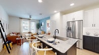 This thoughtfully designed one-bedroom, one-bathroom residence offers an efficient and stylish single-floor layout. The open-concept living and kitchen area forms the heart of the unit, where light wood-tone flooring, recessed lighting, and a ceiling fan create a bright, welcoming atmosphere. The kitchen is a standout feature, showcasing a two-tone design with crisp white upper cabinetry and dark lower cabinets, granite countertops, stainless steel appliances including a French door refrigerator, a built-in microwave, and a range. A central island with seating provides additional prep space and casual dining. The living room receives ample natural light through large windows and a glass door opening to a private balcony. The bedroom features large windows, light wood flooring, and an accent wall, offering a comfortable and functional retreat. The full bathroom includes a granite-topped vanity with dark cabinetry, tile flooring, and direct access to a spacious walk-in closet with built-in shelving and hanging rods. An in-unit laundry area accommodates a full-size washer and dryer, adding everyday convenience.